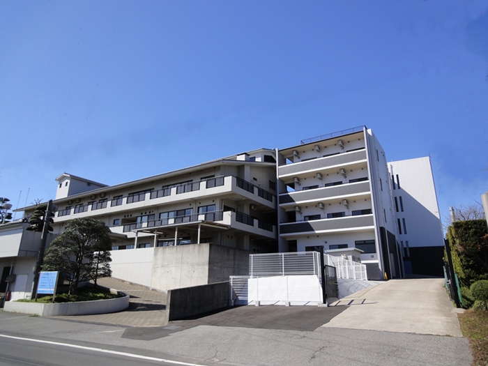 介護施設の建物外観。複数階建ての白とグレーの近代的な建築。